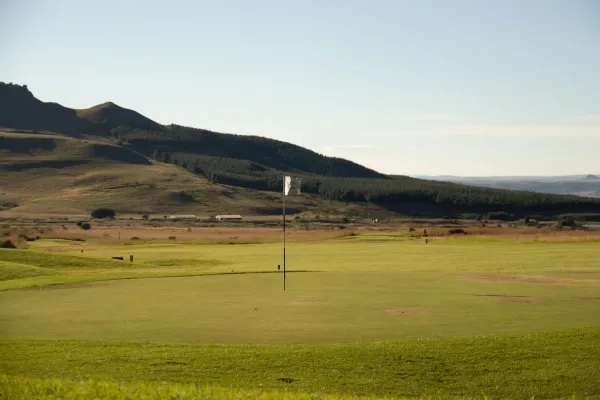 A green golf fairway with mountains in the background.