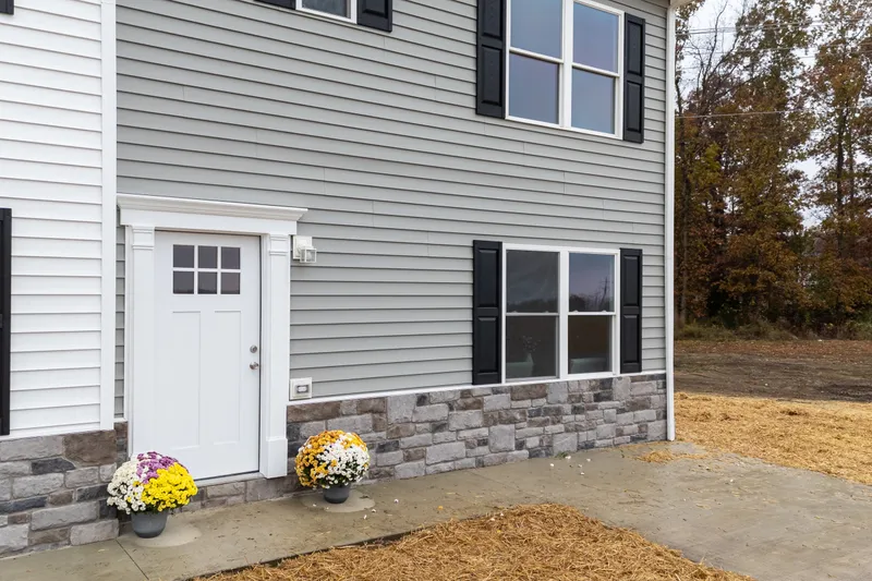 Front porch detail with potted mums, white craftsman door, and stone-veneer base