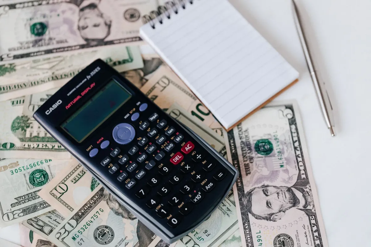 A calculator and notepad placed over U.S. dollar bills.