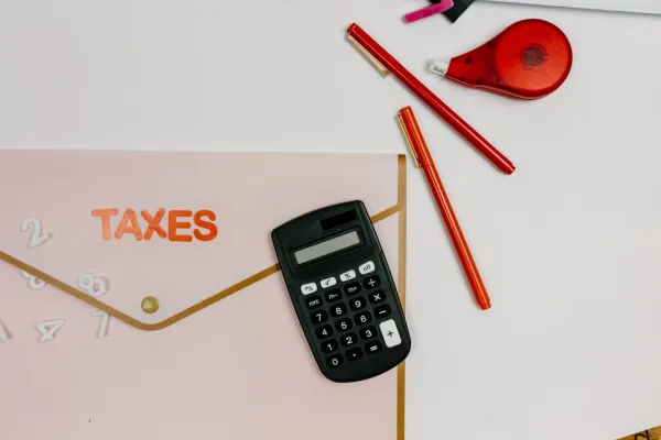 A calculator, pens, and a folder labeled taxes on a flat surface.